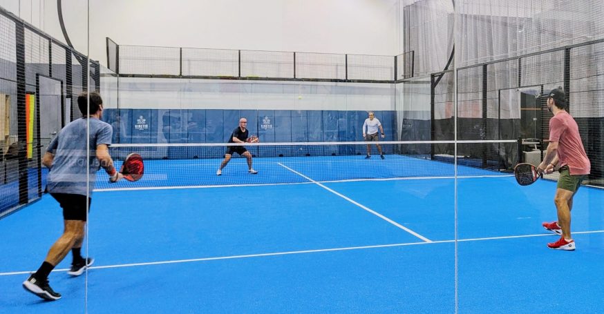 Four padel players contest a point on an indoor court