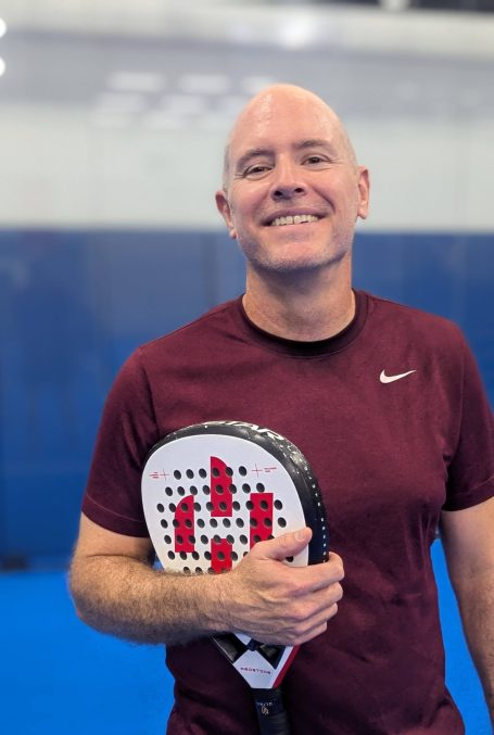 A padel player poses on the court with a racquet
