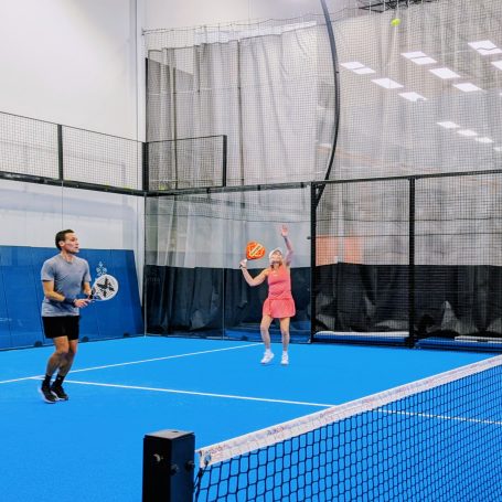 A padel player prepares for an overhead smash as her partner keeps an eye on the opponents
