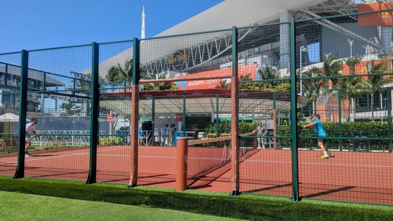 Two players contest a point on a padel court at the 2025 Miami Open tennis tournament with Hard Rock Stadium on the background 