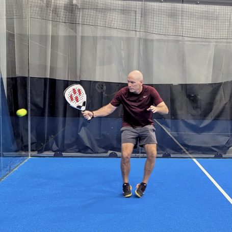 A padel player takes a forehand off a back-wall rebound