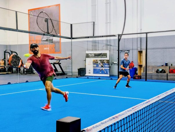 A player in red reaches out for a forehand volley as his partner watches on