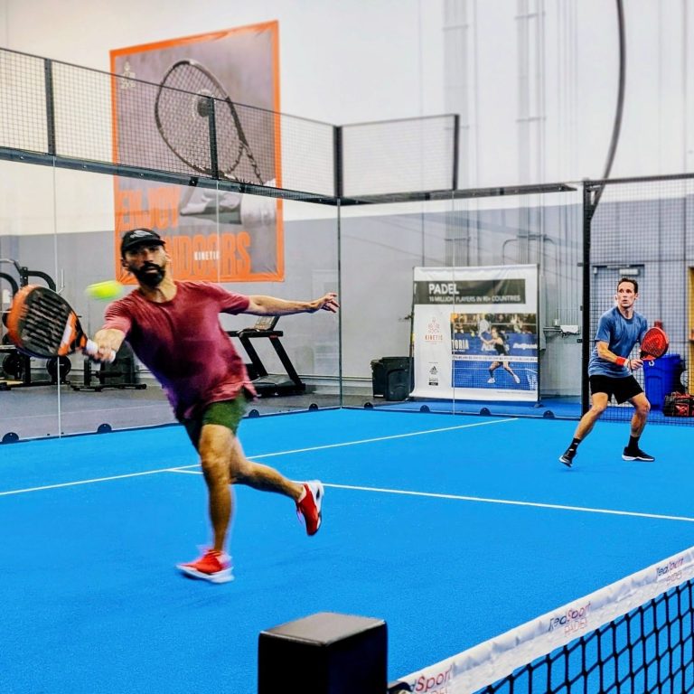 A player in red stretches out for a forehand volley as his partner watches on